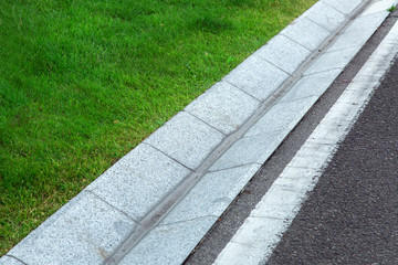 Fototapeta premium Street gutter of a stormwater drainage system on the side of an pedestrian walkway with markings and grass.