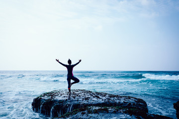 Young woman practice yoga at the seaside coral cliff edge