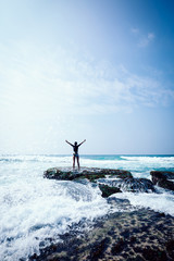 Cheering woman outstretched arms at seaside mossy coral reef