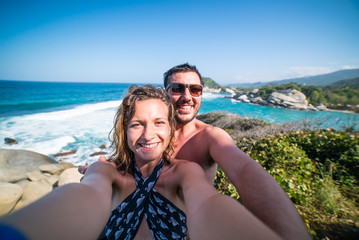 happy smiling couple taking selfie photo in front of the sea in Tayrona National Park, Tropical Colombia. Crazy tourists travelling on the white beach of jungles on caribbean sea. 