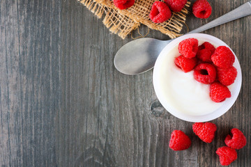 Yogurt with raspberries. Above view corner border on a rustic gray wood background. Copy space.