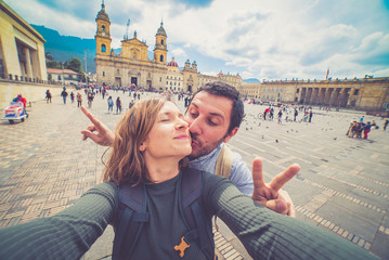 Happy beautiful tourist couple taking a selfie photo in Bogota, Colombia. in the main square of the city called Bolivar square - obrazy, fototapety, plakaty