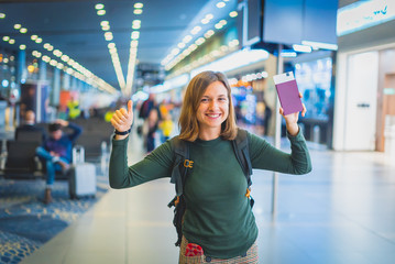 Beautiful young tourist girl in international airport, taking selfie with passport and boarding pass ready for boarding and fly. Doing gesture 