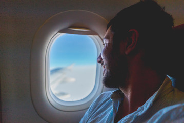 Fototapeta na wymiar handsome man passenger traveler looking at window in airplane, travel by flight, man tourist sitting in air plane watching outside 