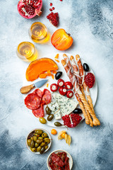Appetizers table with antipasti snacks and wine in glasses. Authentic traditional spanish tapas set, cheese and meat platter over grey concrete background. Top view