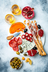 Appetizers table with antipasti snacks and wine in glasses. Authentic traditional spanish tapas set, cheese and meat platter over grey concrete background. Top view