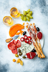 Appetizers table with antipasti snacks and wine in glasses. Authentic traditional spanish tapas set, cheese and meat platter over grey concrete background. Top view
