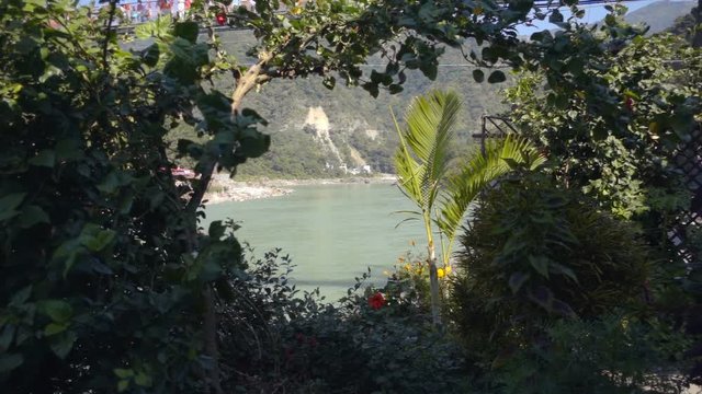 The legendary, sacred Ganges River in the city of Rishikesh, India. View through green spaces and flowers. Suspension bridge over the Ganges in the city of Rishikesh