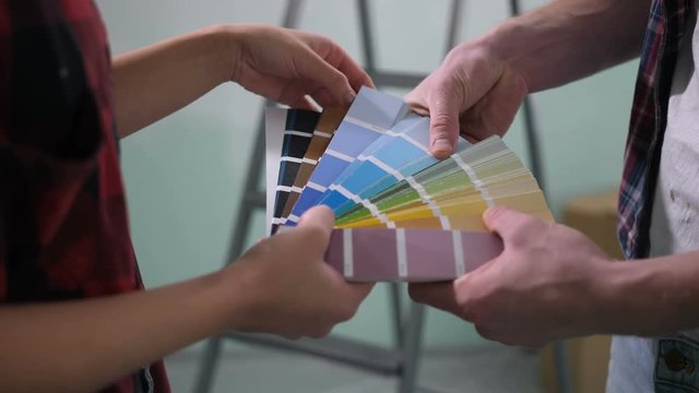 Close-up of couple hands choosing color for painting interior wall from color smaples palette during home renovation. Multi ethnic diy family making decision together about color of house interior.