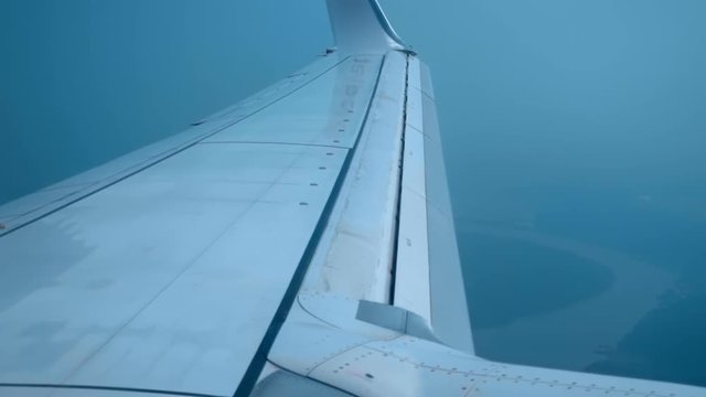 The wing of the aircraft and the red turbine at the time of landing, the slats came out, the flight speed decreases, the outlines of the approaching earth are visible