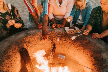 Friends roasting marshmallows for s'mores - obrazy, fototapety, plakaty