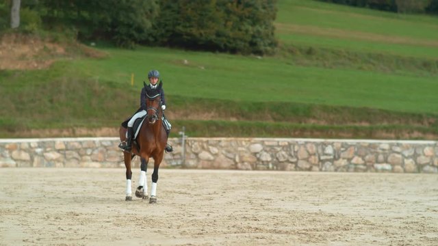 SUPER SLOW MOTION: English female rider doing canter renvers at dressage competition. Dressage horseback rider riding canter traver with her big brown horse. Girl horseback rider training her horse.
