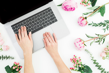 Woman typing on laptop. Office workspace with female hands, laptop, notebook and pink flowers on white background. Top view. Flat lay.