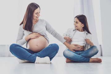Cheerful pregnant woman touching belly of her daughter