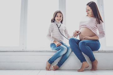 Happy girl listening to baby in mothers belly with stethoscope