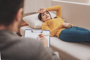 Beautiful stressed woman feeling anxious lying on sofa near therapist