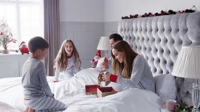 Parents Opening Gifts From Children As They Sit On Bed Exchanging Present On Christmas Day