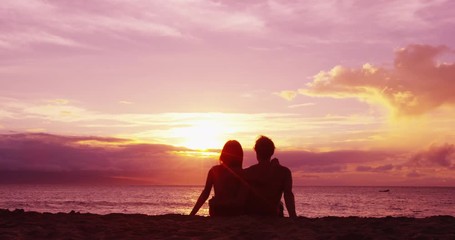 Romantic couple relaxing enjoying on beach looking at sunset with beautiful light and colors. Young couple on honeymoon enjoying travel vacation summer holidays on beach. SLOW MOTION RED EPIC. - Powered by Adobe