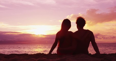 Couple sitting romantic at beach sunset in love at honeymoon vacation travel - Powered by Adobe