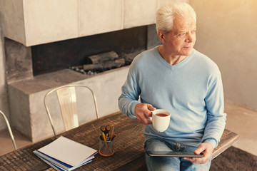 Handsome senior man drinking tea and holding tablet