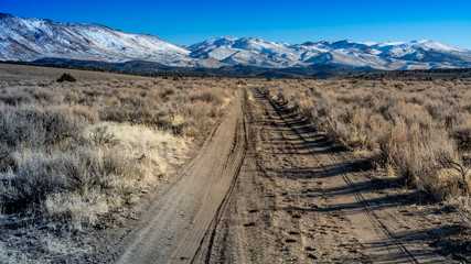 Overview of hIgh desert in Nevada featuring dirt road and snow capped mountain