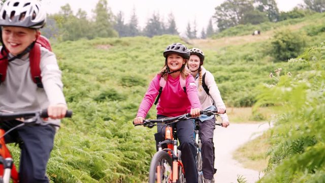 Young family having fun riding mountain bikes on a country lane during a camping holiday, Lake District, UK