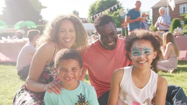 Slow Motion Portrait Of Family With Children Sitting On Rug At Summer Garden Fete