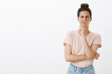 Doubtful and unsure good-looking young female designer with messy bun smirking and frowning as...
