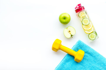 Fototapeta na wymiar Healthy fruit water for sport, fitness. Bottle of water with lemon and cucumber near sport equipment dumbbells on white background top view copy space