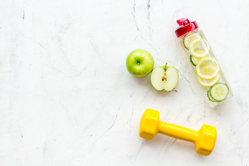 Healthy fruit water for sport, fitness. Bottle of water with lemon and cucumber near sport equipment dumbbells on white stone background top view copy space