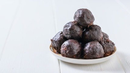 Chocolate-drenched balls of grated nuts and dried fruits in a bowl on a rustic light table.