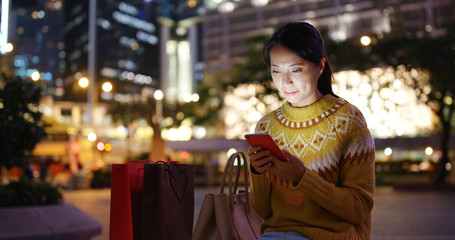 Woman look at the cellphone with shopping bag at night