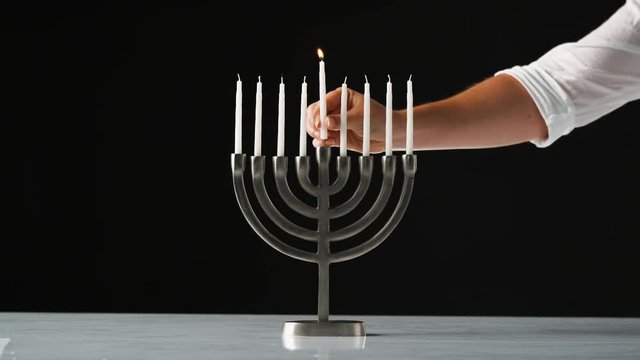 Hand lighting the nine white candles in a Jewish menorah sat on a pale marble surface, close up, front view