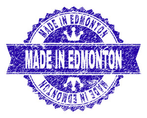 MADE IN EDMONTON rosette stamp imitation with grunge texture. Designed with round rosette, ribbon and small crowns. Blue vector rubber print of MADE IN EDMONTON title with grunge texture.