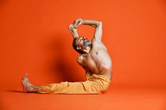 Old man practicing yoga doing stretching exercises against orange background