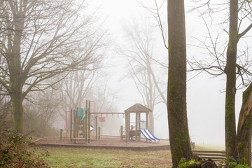 Playground equipment is unused on a damp and foggy morning; fog surrounds a playground on a day too...