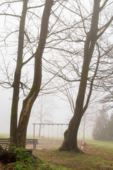 Playground equipment is unused on a damp and foggy morning; fog surrounds a playground on a day too cold for children to play