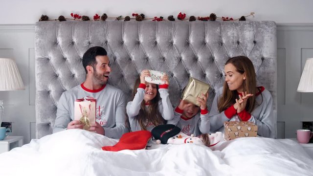 Excited Family In Bed At Home Together Opening Gifts On Christmas Day
