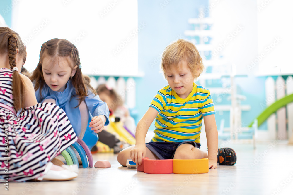 Poster children playing wooden toys at day care center, kindergarten or nursery