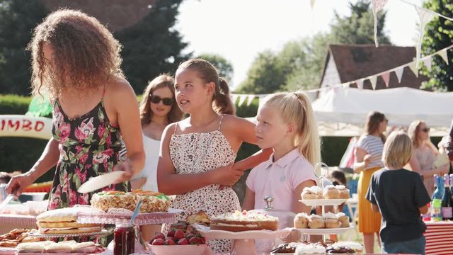 Children Serving On Cake Stall At Busy Summer Garden Fete