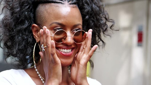 Happy young black woman playing with her sunglasses and laughing, close up