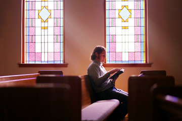 Christian Man Sitting Alone in Dark Empty Church Pew by Bright Stained Glass Window