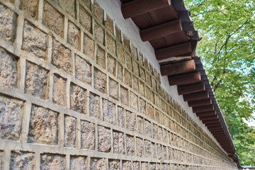 Wall of Deoksu palace in Korea with tiled stones and many brown wooden frames supporting the traditional kiwa.