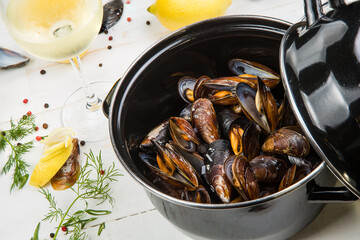 mussels in white wine sauce with glass of white wine , decorated with herbs, lemon and pepper