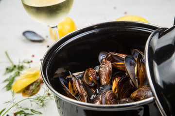 mussels in white wine sauce with glass of white wine , decorated with herbs, lemon and pepper