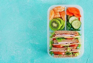 Zelfklevend Fotobehang Schoollunchdoos met sandwich, groenten, water en fruit op tafel. Gezonde eetgewoonten concept. Plat leggen. Bovenaanzicht © timolina