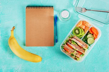 Gordijnen Schoollunchdoos met sandwich, groenten, water en fruit op tafel. Gezonde eetgewoonten concept. Plat leggen. Bovenaanzicht © timolina
