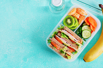 School lunch box with sandwich, vegetables, water, and fruits on table. Healthy eating habits concept. Flat lay. Top view