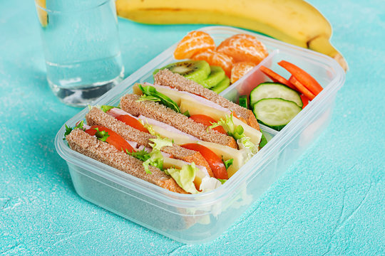School lunch box with sandwich, vegetables, water, and fruits on table. Healthy eating habits concept.