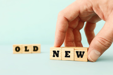 man hand picking wooden cubes with the text NEW over wooden cubes with the text OLD.